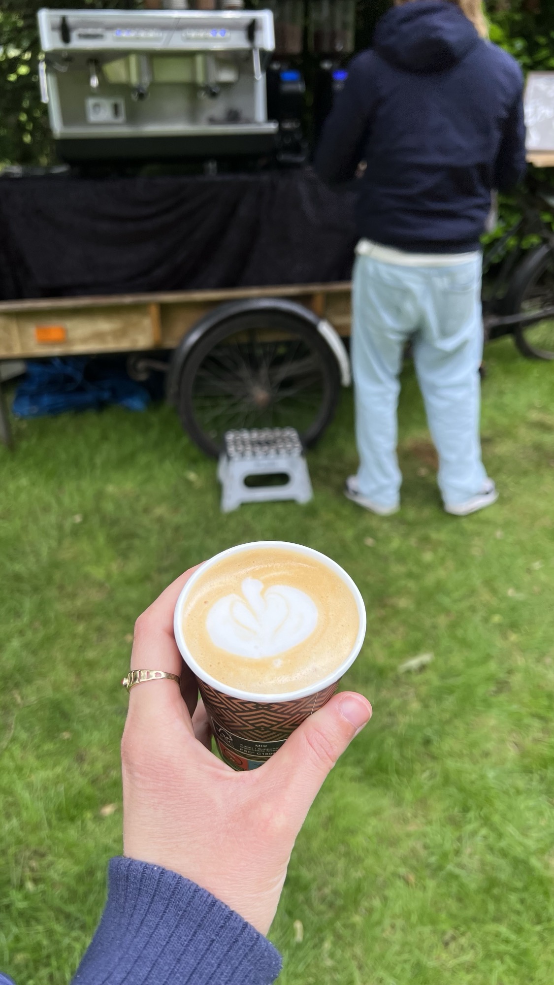 Hand met een kopje koffie met latte art, koffiekar van Absoluukt op de achtergrond